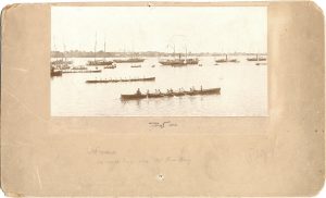 Men rowing racing shells; boats in background decorated with flags; spectators on decks of boats. Handwritten on front: "10 oared barge race, Detroit River Navy."